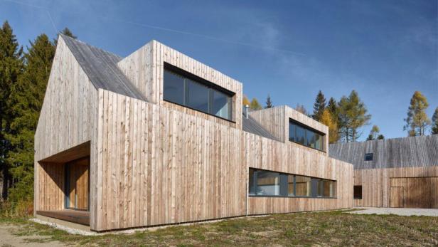Ein modernes Holzhaus mit großen Fenstern vor einem bewaldeten Hintergrund.