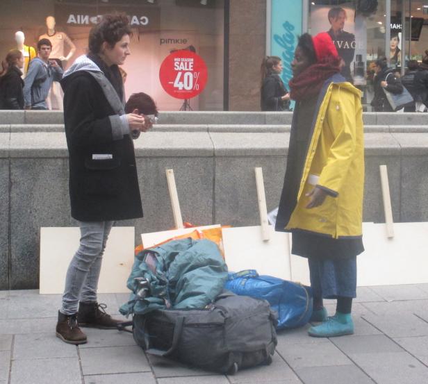 Zwei Frauen stehen vor einem Geschäft mit Gepäck und Schildern.