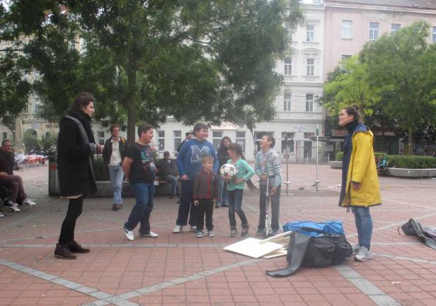 Eine Gruppe von Kindern und zwei Frauen stehen auf einem Platz mit einem Fußball.