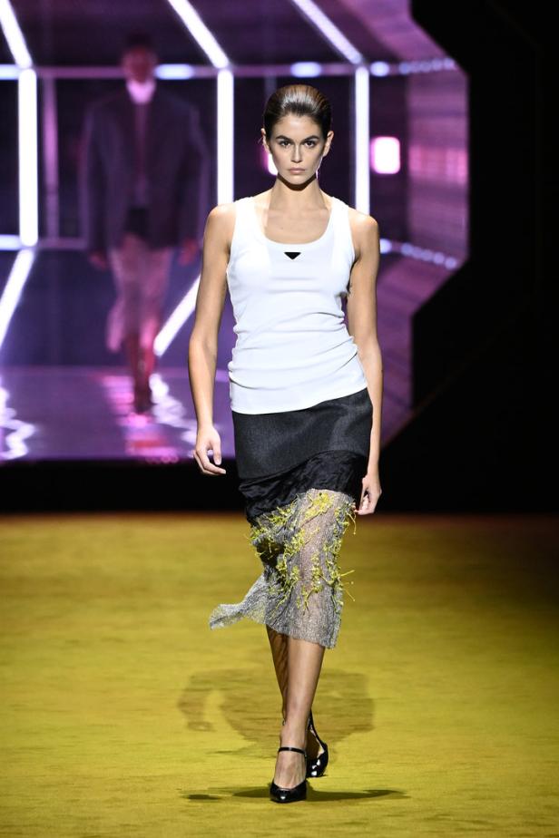 Kaia Gerber läuft in einem weißen Tanktop und einem Rock mit gelben Akzenten über einen Laufsteg.