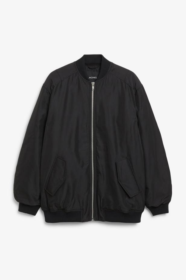 Eine schwarze Bomberjacke mit Reißverschluss hängt vor einem weißen Hintergrund.