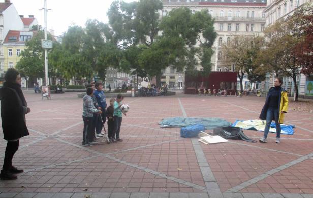 Eine Gruppe Kinder steht auf einem Platz, während eine Frau zusieht.