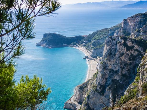 Blick auf eine Küstenlinie mit türkisfarbenem Wasser, Klippen und einem kleinen Strand.