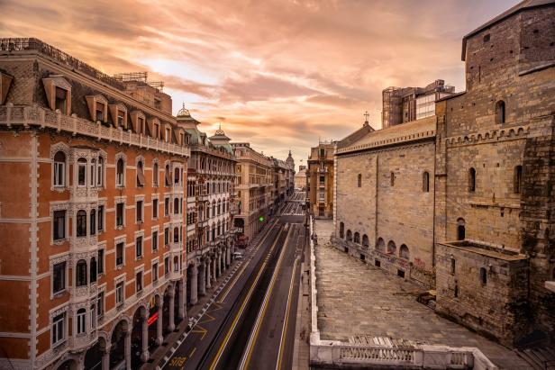 Blick auf eine Straße in Genua, gesäumt von historischen Gebäuden bei Sonnenuntergang.