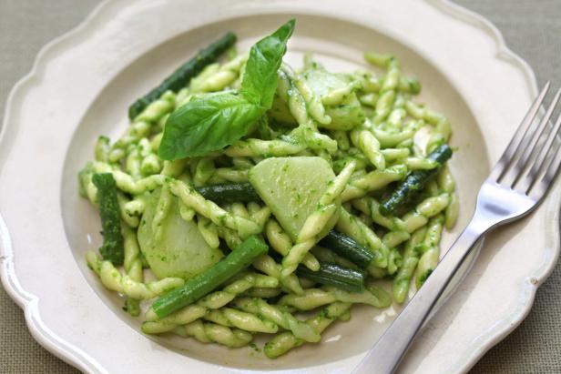 Ein Teller Trofie-Pasta mit Pesto, grünen Bohnen und Kartoffeln, garniert mit Basilikum.