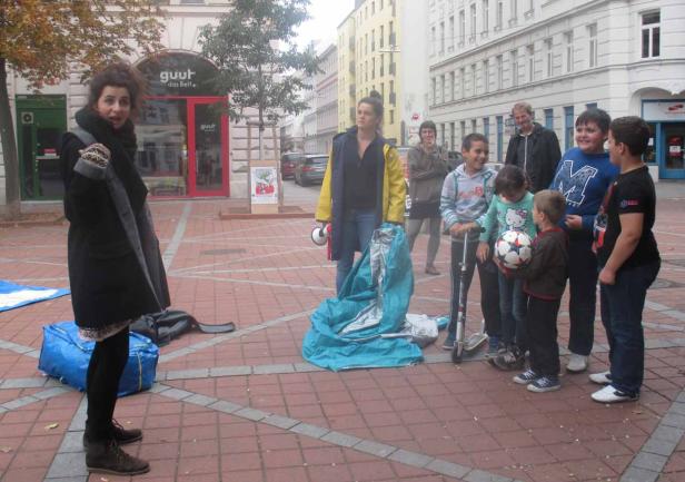 Eine Gruppe von Menschen steht auf einem Platz in der Stadt, möglicherweise beim Aufbau eines Zeltes.