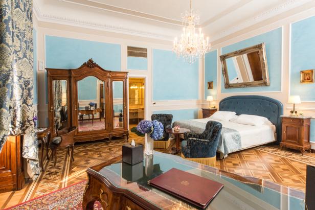Ein luxuriöses Hotelzimmer mit Himmelblau gestrichenen Wänden, einem großen Bett und einem Kristalllüster.