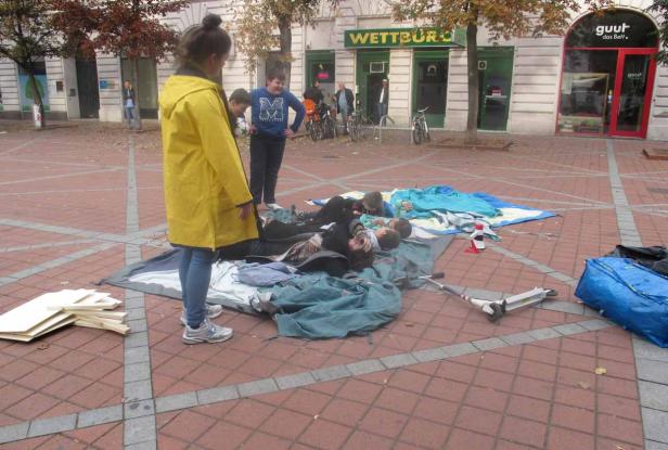 Eine Gruppe von Kindern liegt auf einer Plane auf einem öffentlichen Platz.