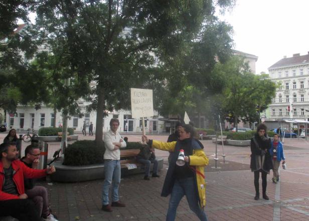 Eine Frau hält ein Schild mit der Aufschrift „Kulturen aller Länder, vereinigt euch“ und spricht in ein Megafon.