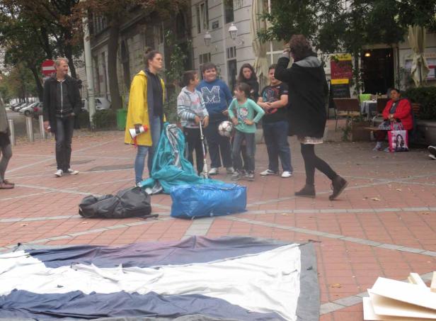Eine Gruppe von Menschen steht auf einem Platz mit einer ausgebreiteten Plane und Gepäckstücken.