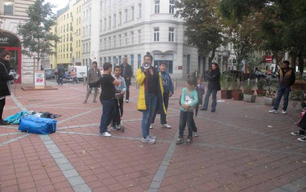 Eine Frau spricht durch ein Megaphon zu einer Gruppe von Kindern auf einem Platz.