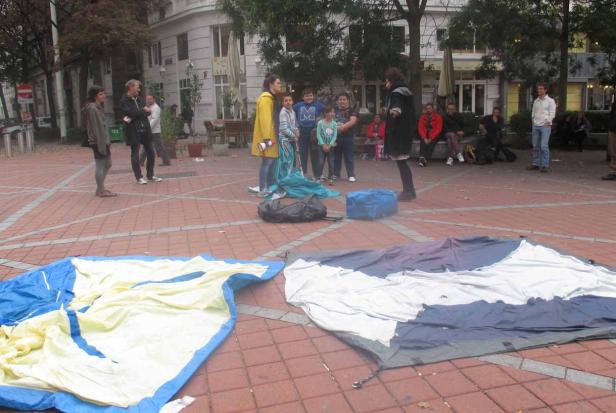 Auf einem Platz liegen zwei ausgebreitete Zelte, umgeben von Menschen.