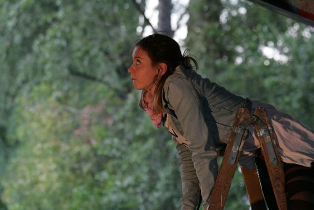 Eine junge Frau steht auf einer Leiter und schaut nach oben.