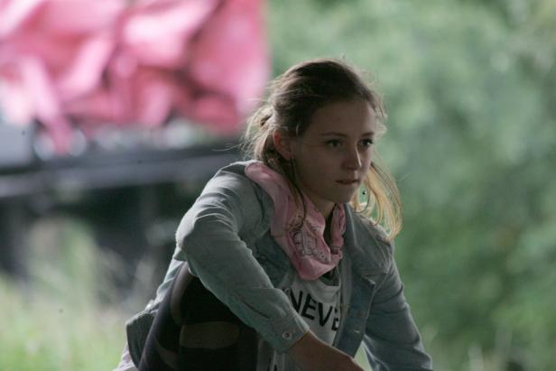 Eine junge Frau mit Jeansjacke und Halstuch blickt nachdenklich zur Seite.