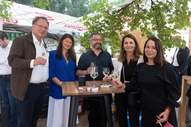 Eine Gruppe von fünf Personen steht an einem Tisch und trinkt Wein.
