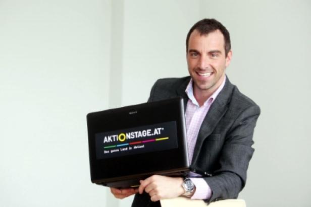 Ein Mann im Anzug hält einen Laptop mit dem Logo von aktionstage.at.