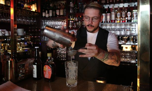 Ein Barkeeper mit Tätowierungen mixt einen Cocktail in einer Bar.