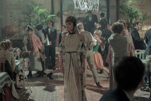 Eine Frau in einem eleganten Kleid steht im Mittelpunkt einer lebhaften Party im Stil der 1920er Jahre.