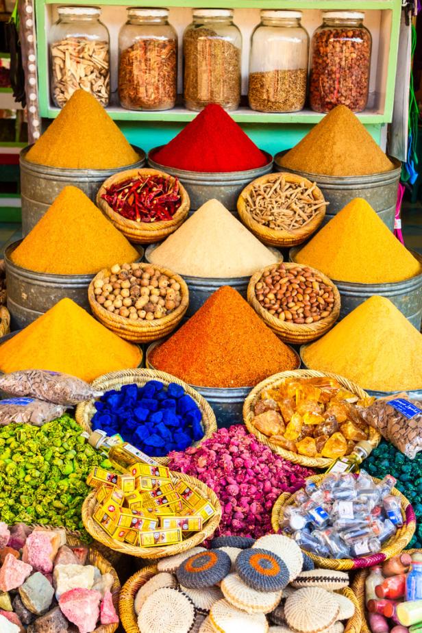 Ein farbenfroher Marktstand mit Gewürzen, Blüten und anderen Waren in Körben und Gläsern.