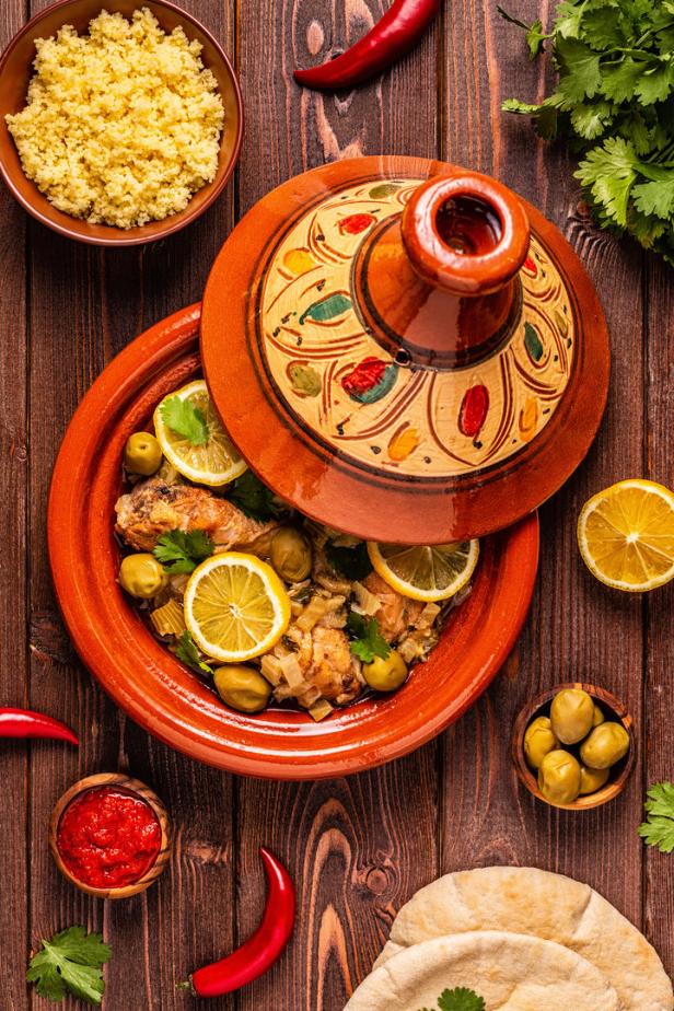 Ein Tajine-Gericht mit Huhn, Oliven und Zitrone wird auf einem Holztisch serviert.