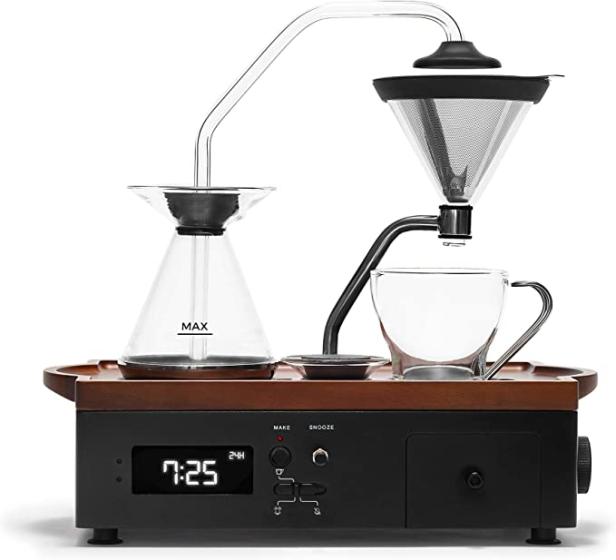 Eine Kaffeemaschine mit Glasbehältern und einer Tasse auf einer Holzbasis mit digitaler Anzeige.