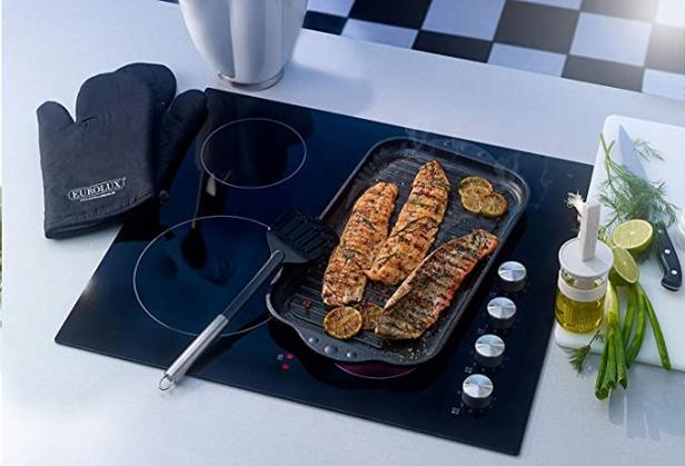 Auf einem Kochfeld steht eine Grillpfanne mit Fisch und Zitronenscheiben.
