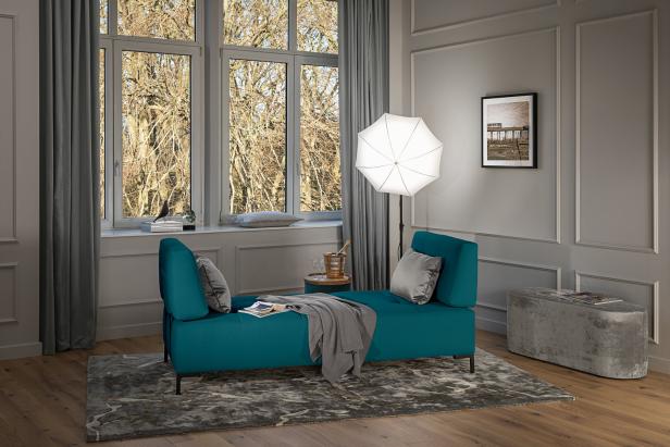 Ein türkisfarbenes Sofa mit Kissen in einem eleganten Wohnzimmer mit grauen Wänden und einem großen Fenster.