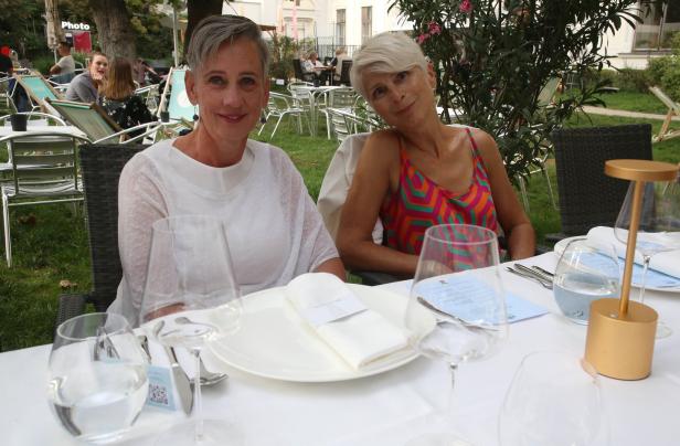 Zwei Frauen sitzen an einem gedeckten Tisch im Freien.