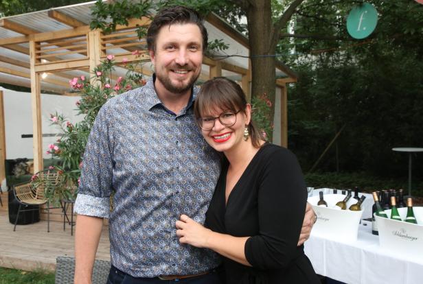 Ein Mann und eine Frau posieren lächelnd vor einem Tisch mit Weinflaschen.