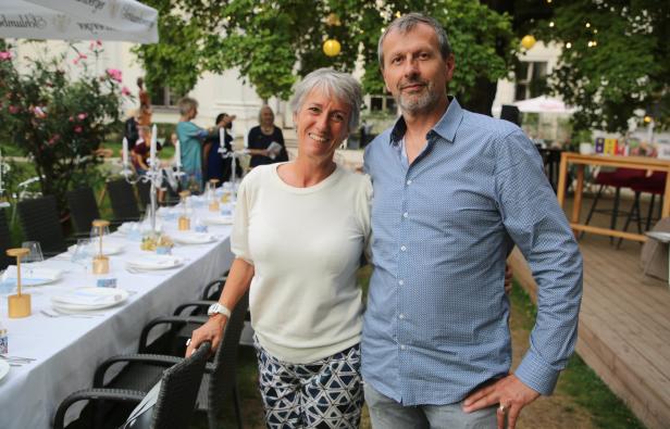 Ein Mann und eine Frau posieren lächelnd vor einer festlich gedeckten Tafel im Freien.