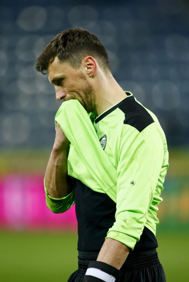 Ein enttäuschter Fußballspieler in Sportkleidung hält sein Trikot vor das Gesicht.