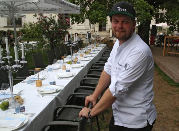 Ein Koch steht an einem langen, gedeckten Tisch im Freien.