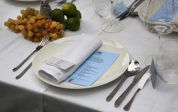 Ein gedeckter Tisch mit Tellern, Besteck, Gläsern, einer Serviette und Obstdekoration.