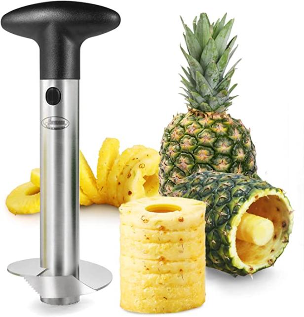 Ein Ananasschneider aus Edelstahl neben einer Ananas und Ananasscheiben.