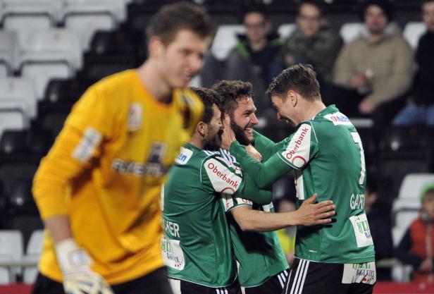 Fußballspieler in grünen Trikots feiern ein Tor, während ein Torwart im Hintergrund steht.