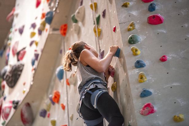 Eine junge Frau klettert an einer bunten Kletterwand in einer Halle.