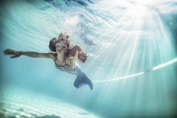 Ein Mädchen, verkleidet als Meerjungfrau, schwimmt mit einer Taucherbrille unter Wasser.
