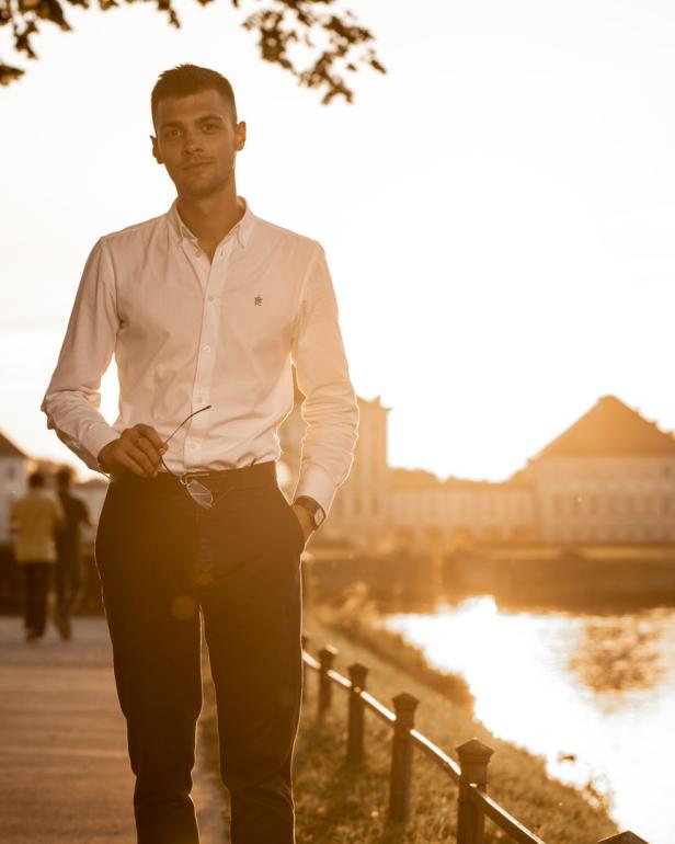 Ein Mann mit Hemd und Hose steht vor dem Schloss Nymphenburg im goldenen Abendlicht.