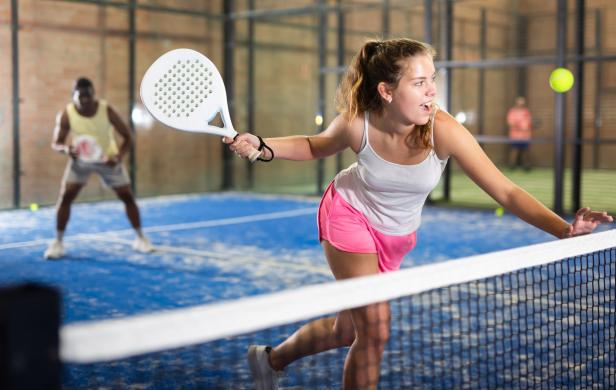 Eine junge Frau spielt Padel-Tennis auf einem blauen Platz.
