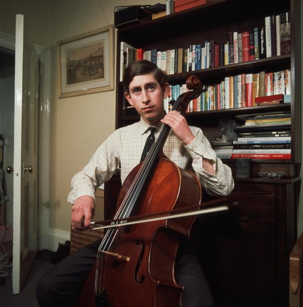 Prinz Charles spielt Cello vor einem Bücherregal.