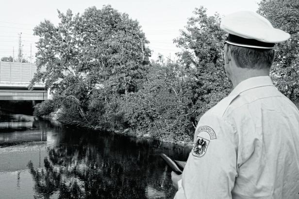 Ein Bundespolizist steht an einem Fluss unter einer Brücke.
