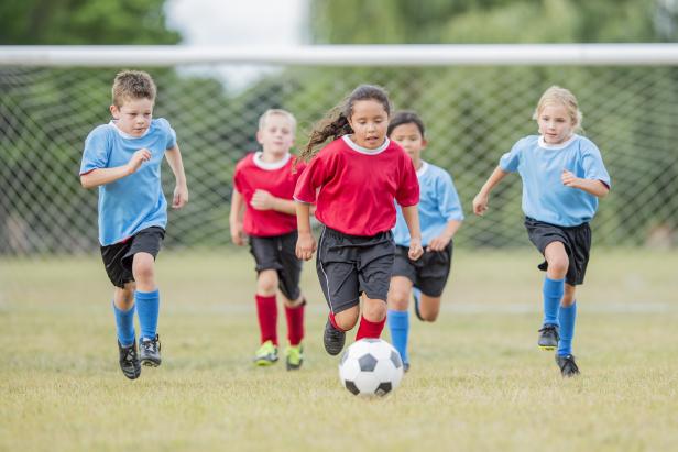 Fünf Kinder spielen Fußball auf einem Rasenplatz und rennen zum Ball.