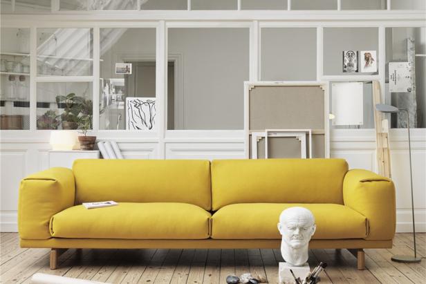 Ein gelbes Sofa steht in einem hellen Raum mit Holzboden und Kunstgegenständen.
