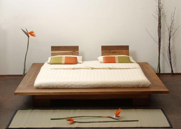 Ein minimalistisches Holzbett mit zwei Kissen und Paradiesvogelblumen als Dekoration.
