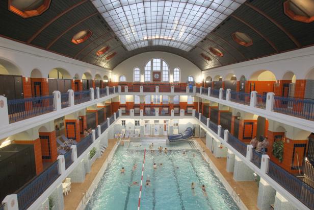 Blick von oben auf ein Schwimmbad mit mehreren Ebenen und Badegästen.