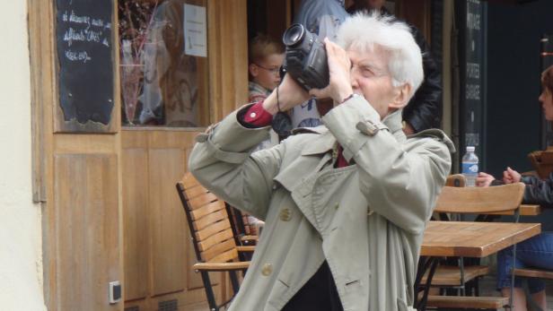 Eine ältere Frau filmt mit einer Videokamera vor einem Café.
