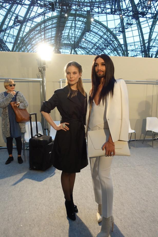 Zwei Frauen posieren vor einem hellen Hintergrund, eine davon ist Conchita Wurst.