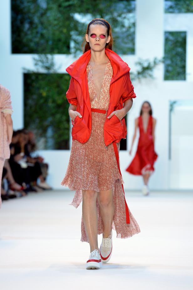 Eine Frau in einem roten Outfit und weißen Schuhen läuft auf einem Laufsteg.