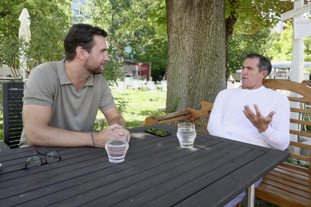 Zwei Männer sitzen an einem Tisch im Freien und unterhalten sich.