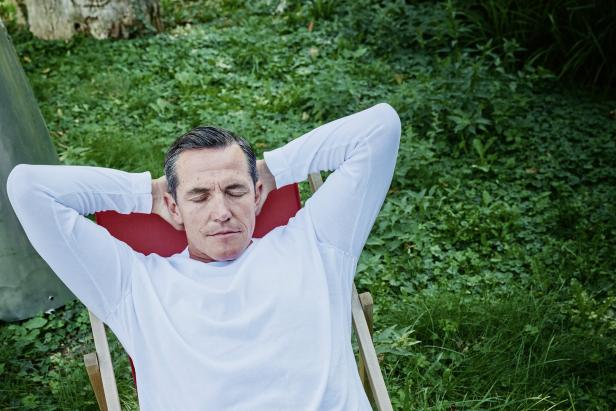 Ein Mann entspannt mit geschlossenen Augen in einem Liegestuhl im Grünen.